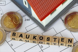 Symbolic image of construction costs: model house with bay letter cubes