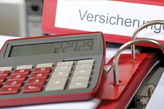 Symbolic image: Folder with insurance policies and calculator on a desk