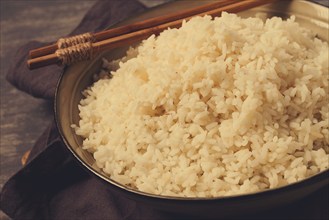 A plate of boiled rice, with wooden sticks, on a brown background, no people, selective focus,