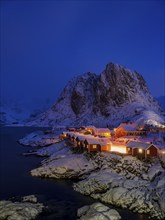 Rorbuer huts of Hamnoy at the fjord at dusk, snowy mountains in the background, Hamnøy, Reine,