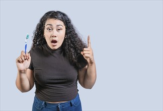 Surprised woman holding toothbrush pointing up. Amazed girl holding toothbrush and pointing up