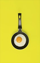 Fried egg, in a small frying pan, on a yellow background, top view