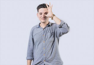 Smiling person making ok gesture looking through fingers isolated. Happy young man making ok