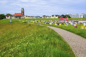 Grassy beach on the dyke with beach chairs and St Peter's Church in the district of Grimmershörn,