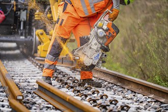 A construction worker cuts tracks with a grinder, sparks fly around, track construction, Hermann