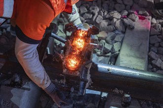 Welding work on a rail with sparks, worker handling tools, intense light, rail welding, track