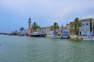 Coastal town with colourful houses and palm trees, boats in the water and a lighthouse, on a sunny