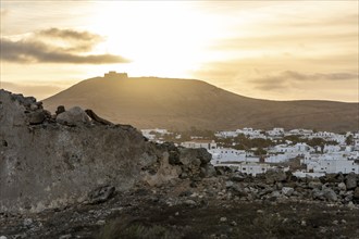 Ruins in the foreground with a view of a white village and hills at sunset, Canary Islands,