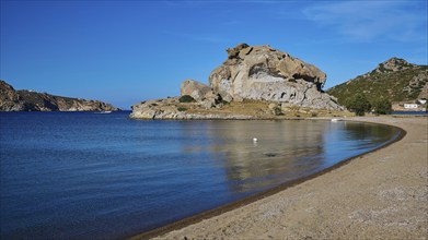 A quiet beach with a rock formation and calm waters under a clear blue sky, Petras Beach,