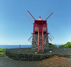 Traditional red windmill Moinho de São João made of volcanic stone in front of a clear blue sky,