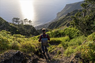 Young man looking out to sea on cliff, evening mood, green coastal landscape on cliff, sea and