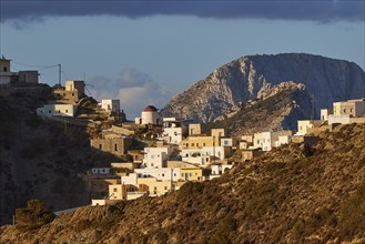 Small houses climb up the mountainside, in the soft light of dusk against a blue sky, Colourful