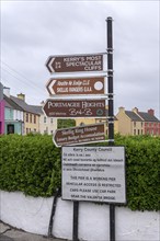 Various signs give directions and clues in a street of colourful houses and grey skies, West Coast,