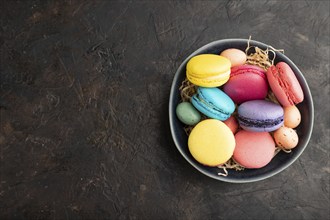 Multicolored macaroons and chocolate eggs in ceramic bowl on black concrete background. top view,