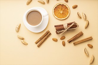 Composition with almonds, cinnamon and cup of coffee on orange pastel background. Blank, flat lay,