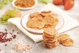 Slices of dehydrated salted meat chips with herbs and spices on gray concrete background and white