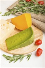 Green basil cheese and various types of cheese with rosemary and tomatoes on wooden board on a