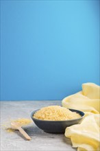 Blue ceramic bowl with raw golden rice and wooden spoon on a gray and blue background and yellow