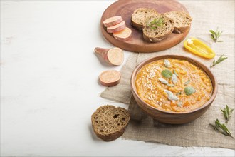 Sweet potato or batata cream soup with sesame seeds in a wooden bowl on a white wooden background