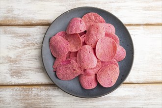 Red potato chips with herbs and tomatoes on white wooden background. Top view, flat lay, close up