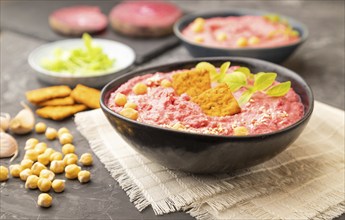 Hummus with beet and microgreen basil sprouts in ceramic bowl on a black concrete background and