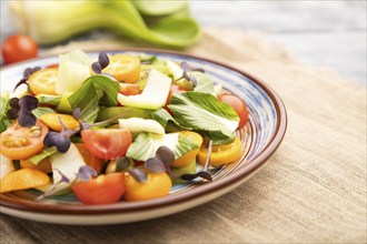 Vegetarian salad of pac choi cabbage, kiwi, tomatoes, kumquat, microgreen sprouts on gray wooden