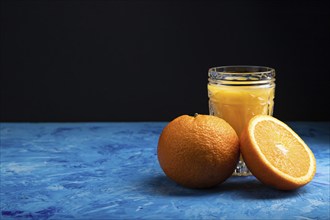 Glass of orange juice on a black and blue background. Hard light, contrast. Side view, copy space