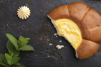 Sour cream bun with cup of coffee on a black concrete background and linen textile. top view, flat