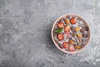 Chocolate cornflakes with milk, strawberry and almonds in ceramic bowl on pastel orange background.