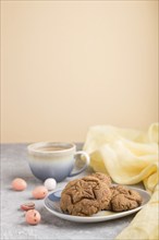 Homemade oatmeal cookies with a cup of cocoa and a yellow textile on a gray and orange background.