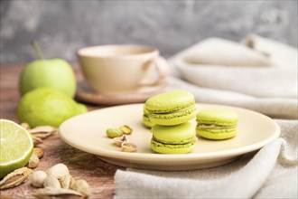 Green macarons or macaroons cakes with cup of coffee on a brown concrete background and linen