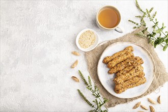 Crumble cookies with seasme and almonds on ceramic plate with cup of green tea and linen textile on