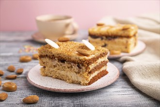 Honey cake with milk cream, caramel, almonds and a cup of coffee on a gray and pink background and