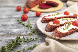 Red beet bread sandwiches with cream cheese and tomatoes on gray wooden background and linen