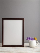 Brown wooden frame mockup with snowdrop crocus flowers on gray paper background. Blank, vertical