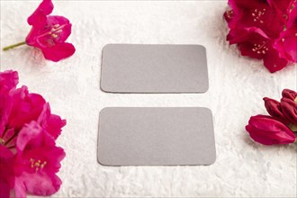 Gray business card with purple azalea flowers on gray concrete background. side view, copy space,