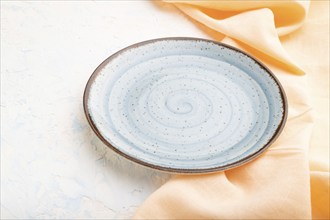 Empty blue ceramic plate on white concrete background and orange linen textile. Side view, close up