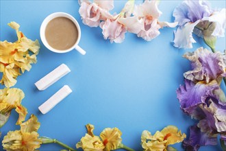 Purple, pink, yellow iris flowers and a cup of coffee on pastel blue background. Morninig, spring,