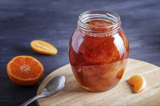 Tangerine and kumquat jam in a glass jar with fresh fruits on a black wooden table. Homemade, copy