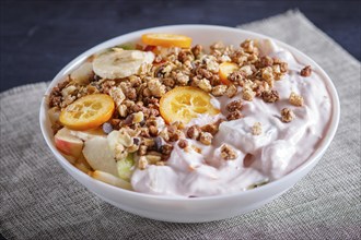 Vegetarian salad of bananas, apples, pears, kumquats, kiwi with granola and yogurt on black woodem