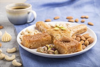 Traditional arabic sweets (basbus, kunafa, baklava), a cup of coffee and nuts on a gray concrete