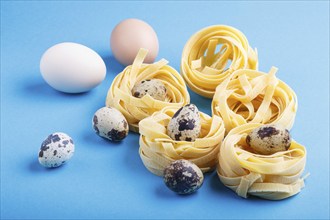 Raw uncooked tagliatelle pasta with quail eggs on a blue pastel background. side view, close up