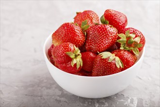 Fresh red strawberry in white bowl on gray concrete background. side view, close up, selective