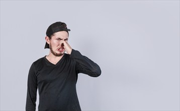 Young man covering nose isolated. Guy with a face of unpleasant odors covering nose