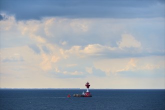 A red lighthouse stands on a calm, blue sea under a slightly cloudy sky, with a pilot boat,