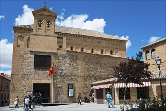 Historic church in Toledo with flag, people strolling and beautiful blue sky and trees in the