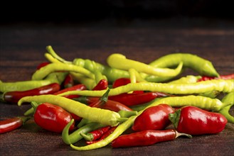 A mixture of green and red peppers lies on a dark wooden surface, food photography