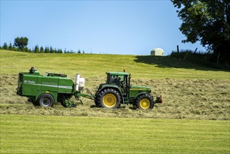 Hay harvest, farmer with agricultural machine, picks up mown hay, which is immediately pressed into