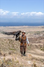 Traditional Kyrgyz eagle hunter hunting in the mountains in a dry landscape, near Kysyl-Suu, Issyk