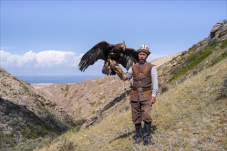 Traditional Kyrgyz eagle hunter with eagle in the mountains, near Kysyl-Suu, Kyrgyzstan, Asia